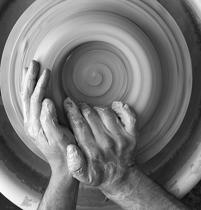 raw clay on a spinning pottery wheel with hands
