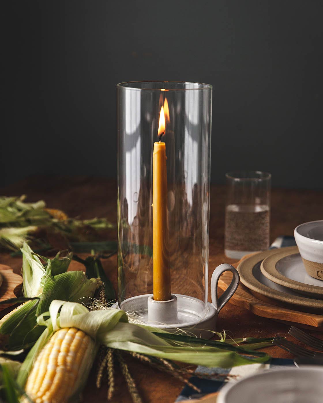 A hand-dipped special blend wax gold taper candles in a handmade pottery hurricane surrounded by corn