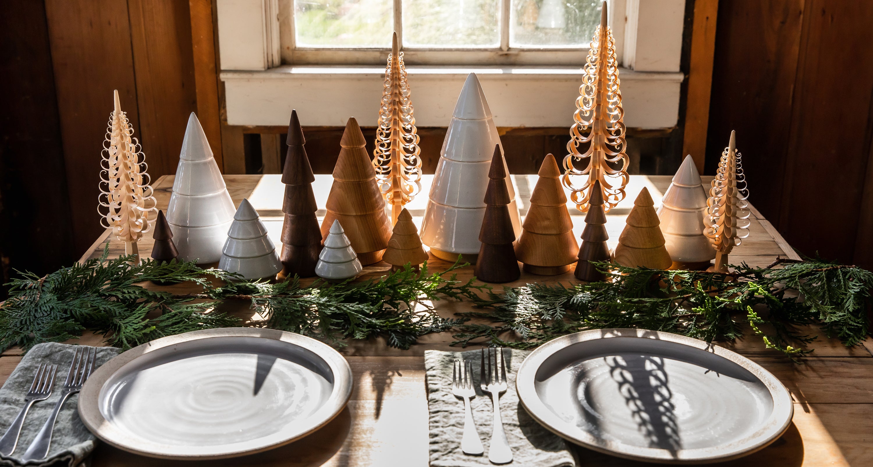Decorative table setting with Christmas tree-shaped candles and greenery on a wooden table.