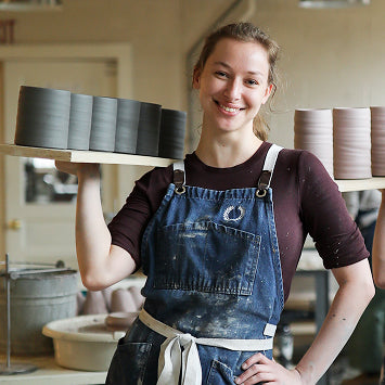 Person wearing a blue apron holding a ceramic item in a workshop.